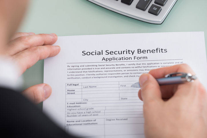 Close-up Of Person Hand Filling Social Security Benefits Form